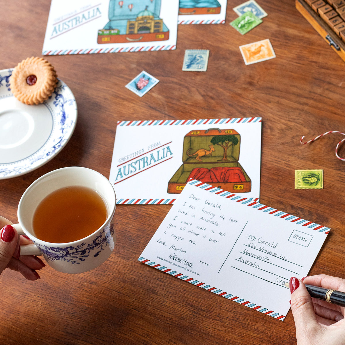 Person holding a cup of tea whilst writing on an Australian postcard.
