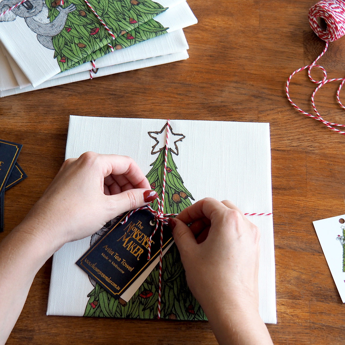 Person tying a string around a Christmas-themed tea towel on a wooden surface