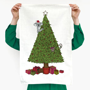 Person holding a towel with a Christmas-themed design of a koala in a tree with presents and a star.