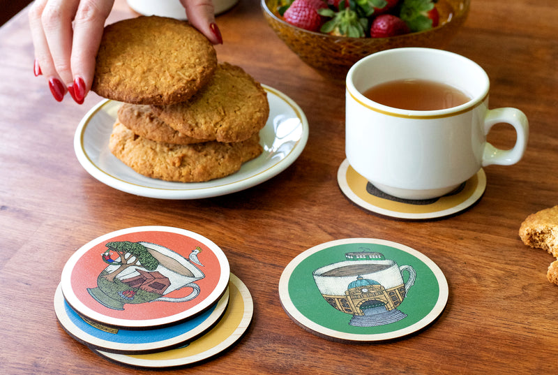 Australian Coasters with teacup themed designs on a wooden table with cookies and a mug of tea.