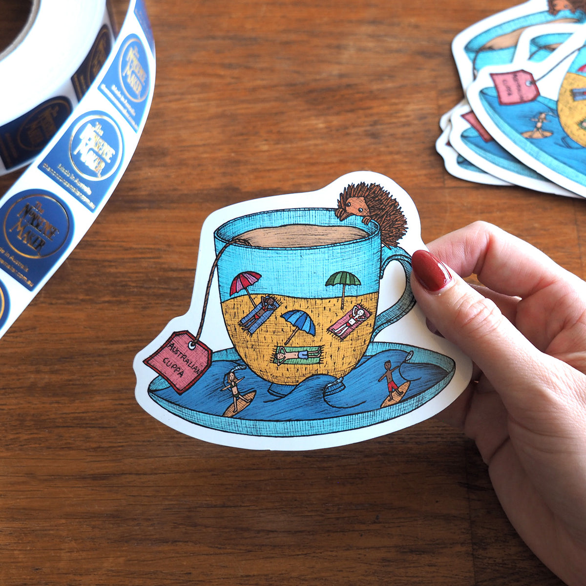 Magnet of a cup with an Australia echidna and beach scene held by a hand on a wooden surface.