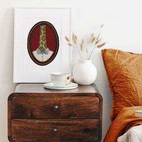 Wooden nightstand with a cup, saucer, and vase, featuring a framed picture of a giraffe on a white wall.