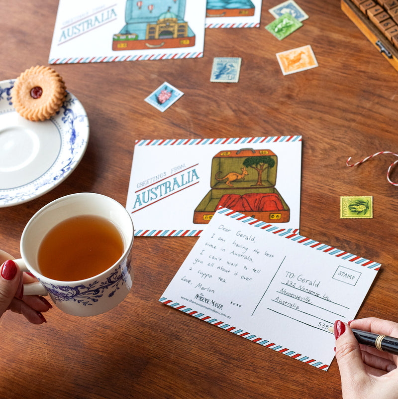 Person holding a cup of tea whilst writing on an Australian postcard.