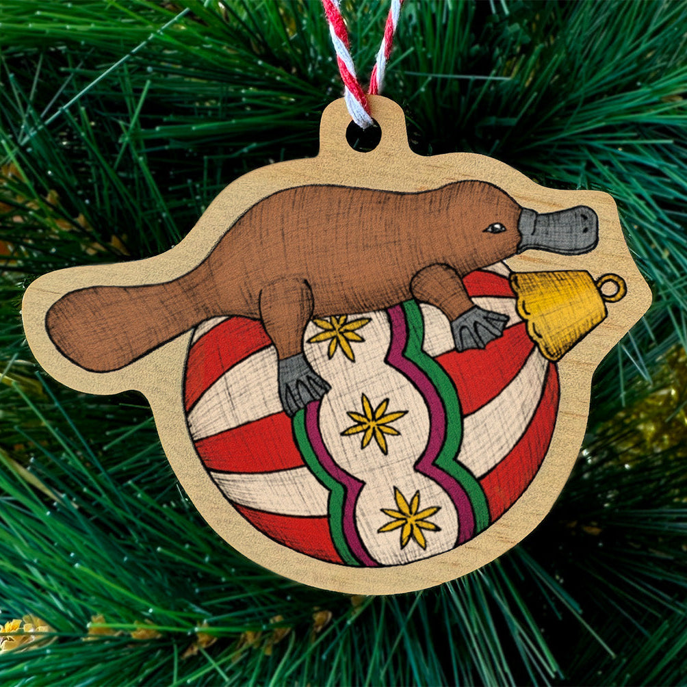 Wooden ornament shaped like a platypus on a Christmas tree with tinsel.