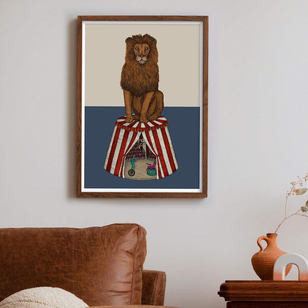 Framed artwork of a lion on a circus tent with a brown armchair and wooden cabinet in the foreground.