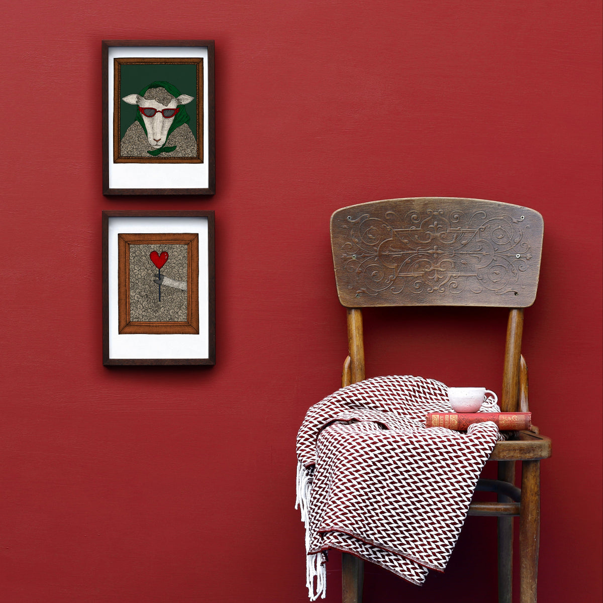 Wooden chair with a patterned blanket against a red wall with two framed artworks of a sheep.