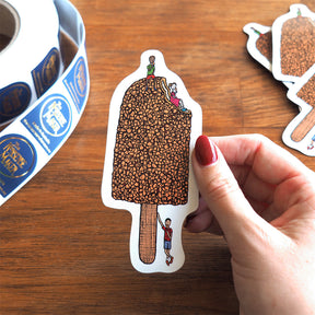 Hand holding a golden gaytime magnet with packaging in the background 